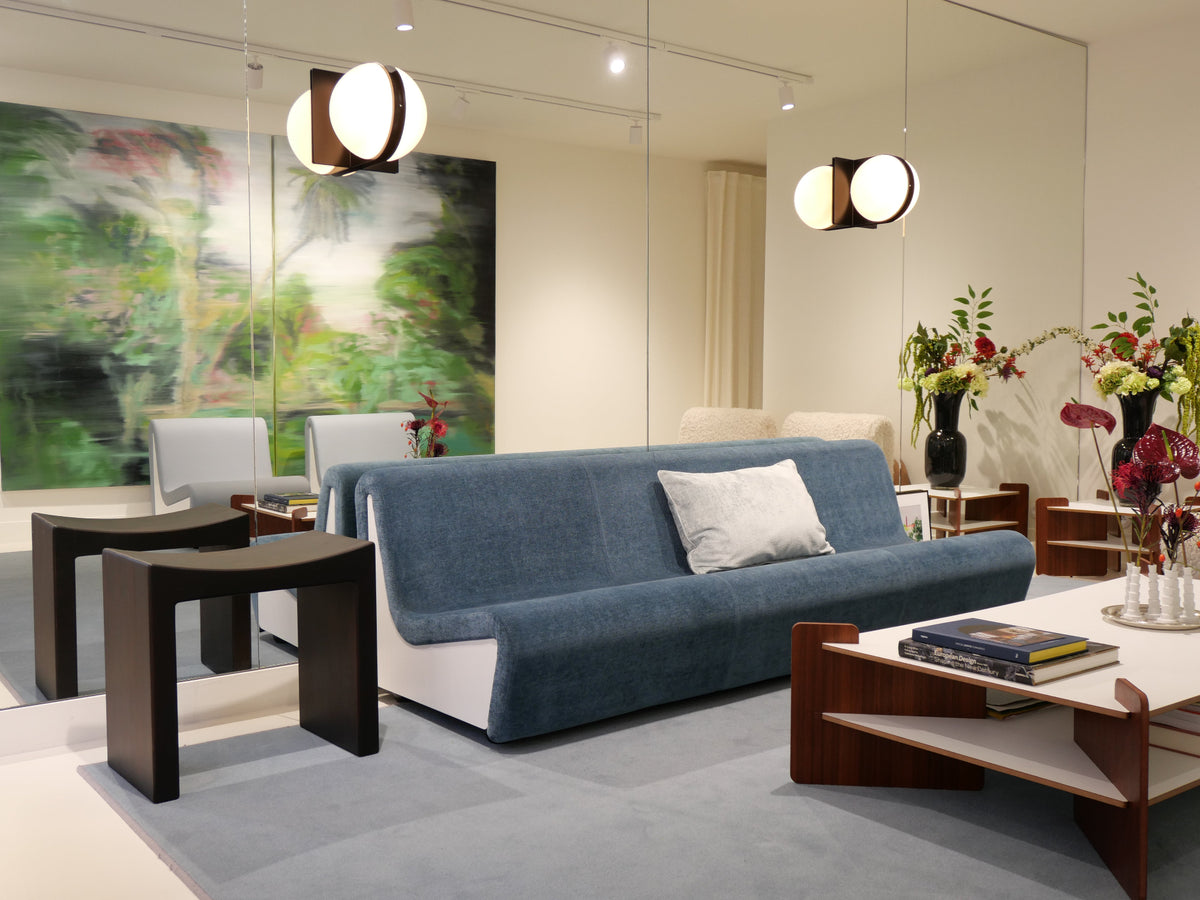 Source Édition showroom in Paris featuring Dialogue Midnight Blue sofa by André Monpoix (1967), TU-TU side and coffee tables in white laminate by Turenne Chevallereau (1968), Basilio stool in solid linden wood with smooth dark finish by Giuseppe Rivadossi (1970), black wall-mounted Jumelles lamp by Ben Swildens (1970), and Miniflore minimalist vases by Claude Courtecuisse (1970)