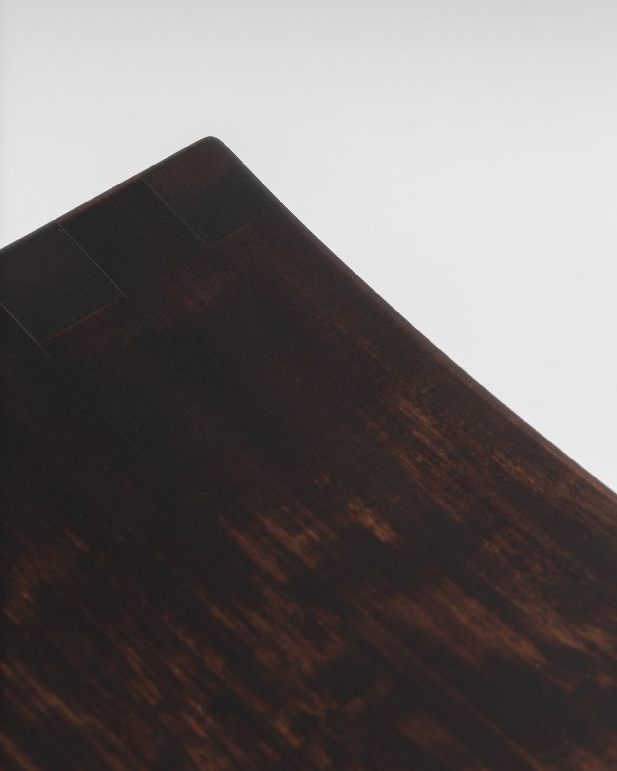 Close-up of the Basilio stool in solid linden wood with dark smooth finish revealing a unique uneven tint effect