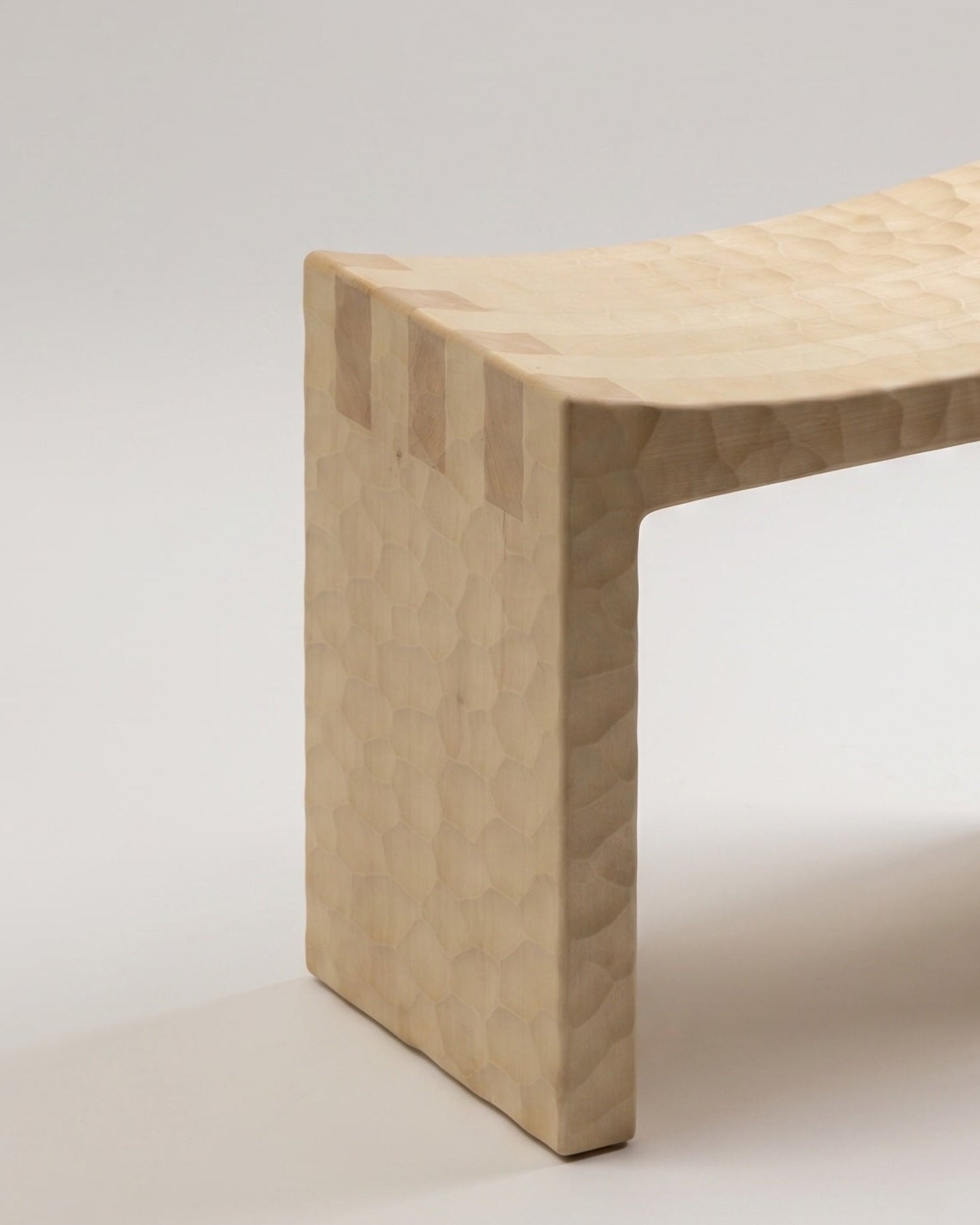 Close-up of the Basilio stool in solid linden wood with natural gouged finish revealing a unique uneven tint effect
