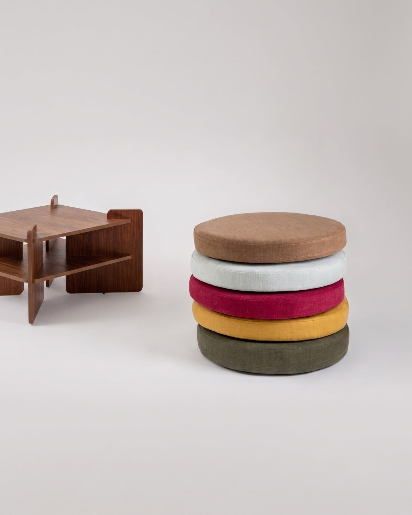 TU-TU side table in walnut veneer, shown as a pouf, with seat cushions stacked beside it in five colors (Arctic Blue, Hazelnut, Curry, Burgundy, Moss) front view