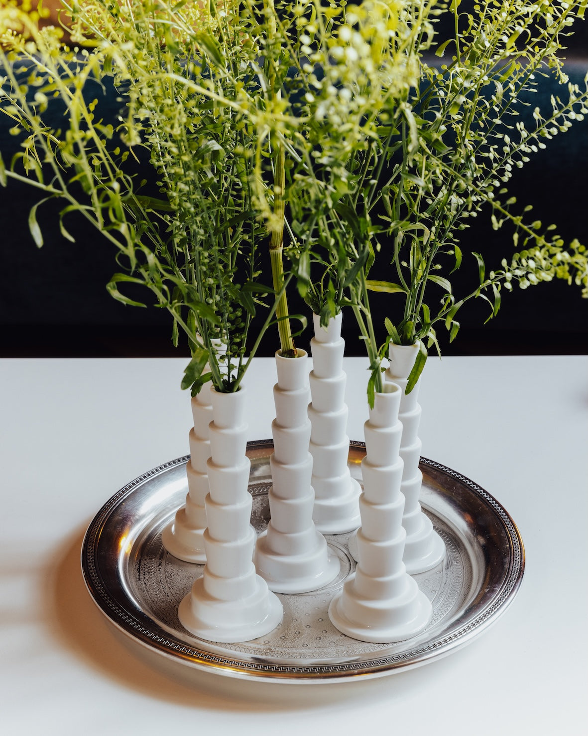 Miniflore porcelain flower holders designed by Claude Courtecuisse in 1970, arranged on a silver tray with delicate green stems and small yellow flowers. Photo by Piergiorgio Sorgetti.